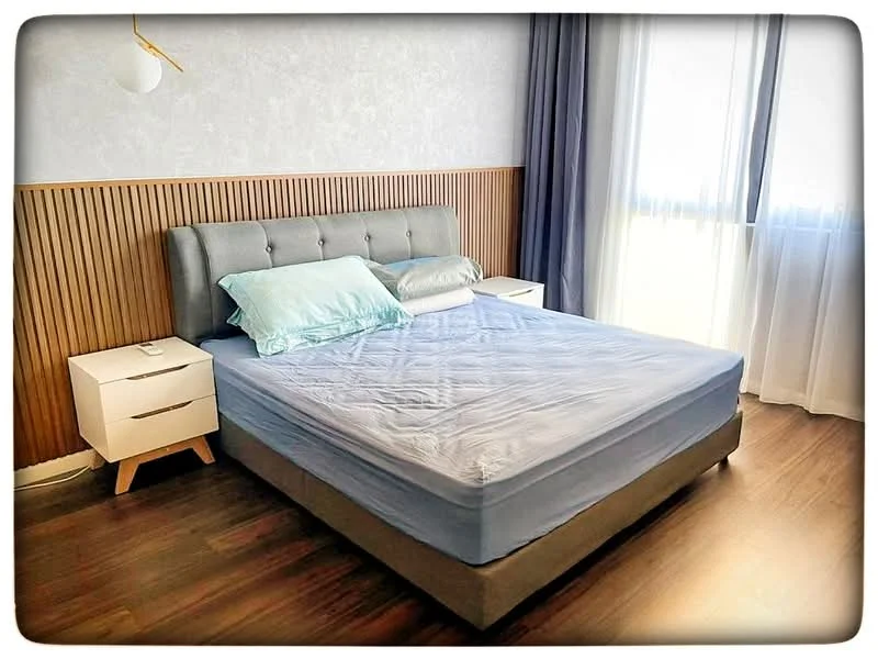 Bedroom features: king-size bed, upholstered headboard, light blue bedding, wooden accent wall, white painted walls, floor-to-ceiling windows, sheer curtains, nightstands with drawers, table lamp, laminate flooring; style: modern.