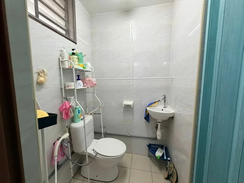Bathroom features: white tiled walls, light grey tiled flooring, one-piece toilet, small pedestal sink, wall-mounted mirror, shower caddy, toilet paper holder, shelf with toiletries, window for natural light, blue towel, yellow sponge, cleaning supplies, plastic storage basket; style: modern.