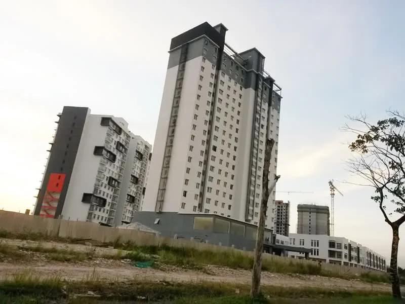 Exterior type: high-rise condominium; features: white painted facade, grey accent panels, glass windows, balconies on upper floors, approximately 20-storey high-rise, surrounded by open land, construction cranes visible, adjacent to other buildings; style: modern.