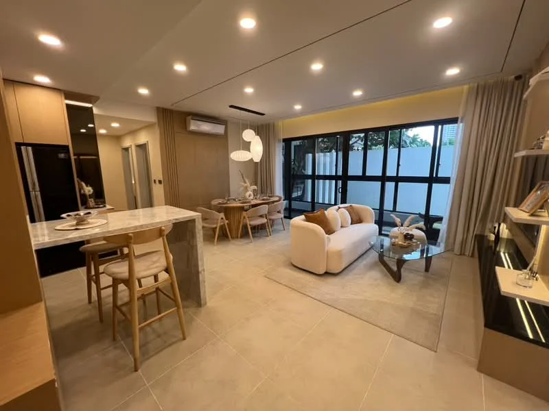 Living features: cream fabric sofa, glass coffee table, wall-mounted TV, built-in shelving unit, recessed LED downlights, large windows with black frames, light beige wall, tile flooring, decorative wall art, area rug, dining table with chairs, kitchen island with seating; style: modern; view: garden.
