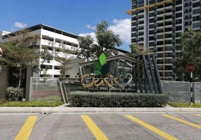 Exterior type: high-rise condominium; features: modern entrance signage, landscaped garden with shrubs, manicured lawn, surrounding trees, glass facade, concrete structure, paved driveway, visible parking structure, gated entry, urban context with clear sky; style: modern.