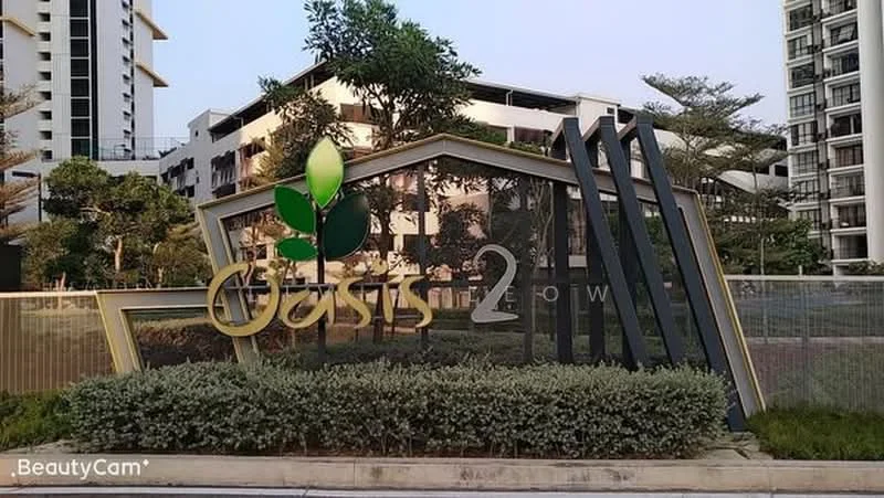 Exterior features: signage with the name 'Oasis 2', green leaf design on signage, landscaped area with shrubs, modern architectural elements, surrounding buildings visible, paved pathway, urban setting; style: modern.