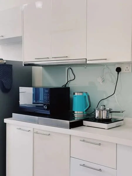Kitchen features: white cabinetry with glossy finish, black countertop, built-in microwave, stainless-steel kettle in turquoise, stainless-steel pot on stove, single-bowl stainless-steel sink, chrome faucet, glass splashback, under-cabinet lighting, wall-mounted power outlet, cooking hob, kitchen towel holder; style: modern.