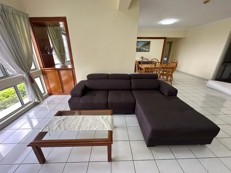 Living features: L-shape sectional sofa in dark brown fabric, glass-top coffee table with wooden frame, white tiled flooring, floor-to-ceiling windows with sheer curtains, built-in wooden shelving unit, neutral painted walls, recessed ceiling lights, dining area visible in background; style: modern; view: garden.