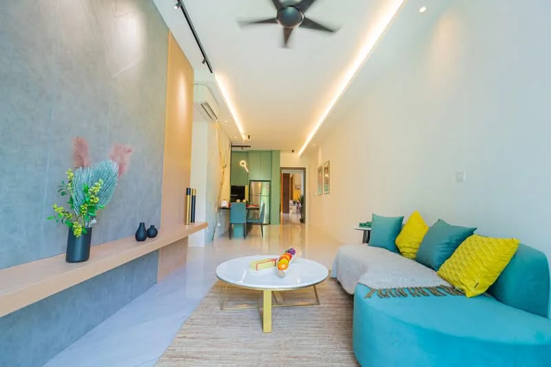 Living features: light grey accent wall, white painted walls, marble flooring, 5-blade ceiling fan with light, sofa in teal fabric, yellow decorative cushions, round coffee table with white top, area rug with natural fibers, wall-mounted shelf, decorative vases, greenery in ceramic pot, recessed LED downlights; style: modern.