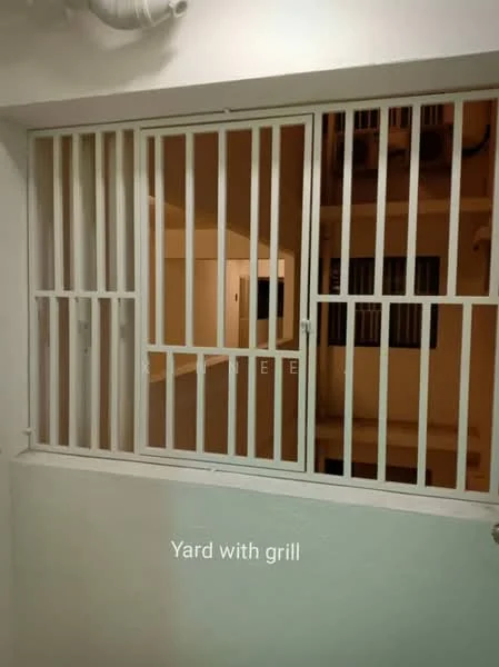 Room features: white painted walls, metal security grille, window with grill, visible yard area.