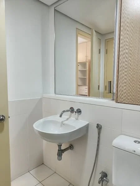 Bathroom features: white ceramic sink, chrome basin mixer faucet, white toilet, mirror above sink, white tiled walls, light-colored flooring, wooden cabinet, shower hose, wall-mounted storage, neutral wall color; style: modern.
