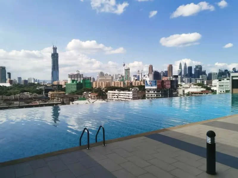 Exterior type: swimming pool deck; features: infinity pool, city skyline view, poolside handrails, paved flooring, outdoor lighting, surrounding urban landscape; style: modern.