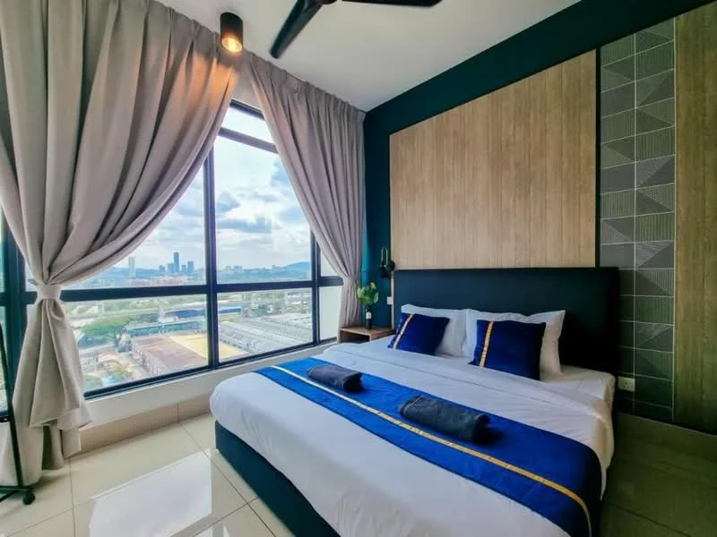 Bedroom features: king-size bed with upholstered headboard, blue and gold bedding, floor-to-ceiling windows, sheer curtains, dark accent wall, wood paneling behind the bed, decorative wall with geometric pattern, nightstands on either side of the bed, table lamp on nightstand, plant on nightstand, tile flooring, ceiling fan with light; style: modern; view: city.