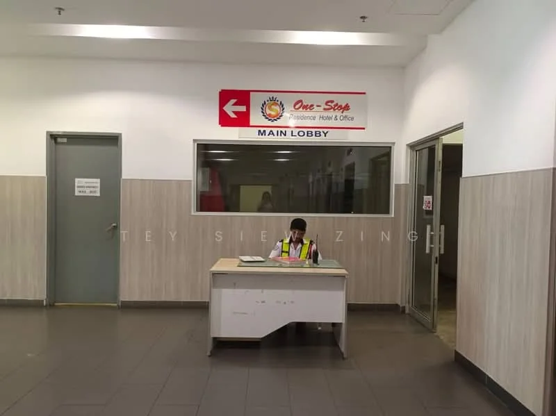Room features: tiled flooring, white painted walls, wood paneling, reception desk, signage for 'Main Lobby', glass window, office chair, person seated at desk, lighting fixtures, doorway, security signage; style: modern.