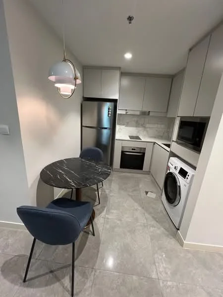 Kitchen features: grey cabinetry, marble countertop, stainless-steel fridge, built-in oven, ceramic cooktop, microwave, washing machine, round dining table, two upholstered chairs, recessed lighting, tile flooring, white backsplash; style: modern.