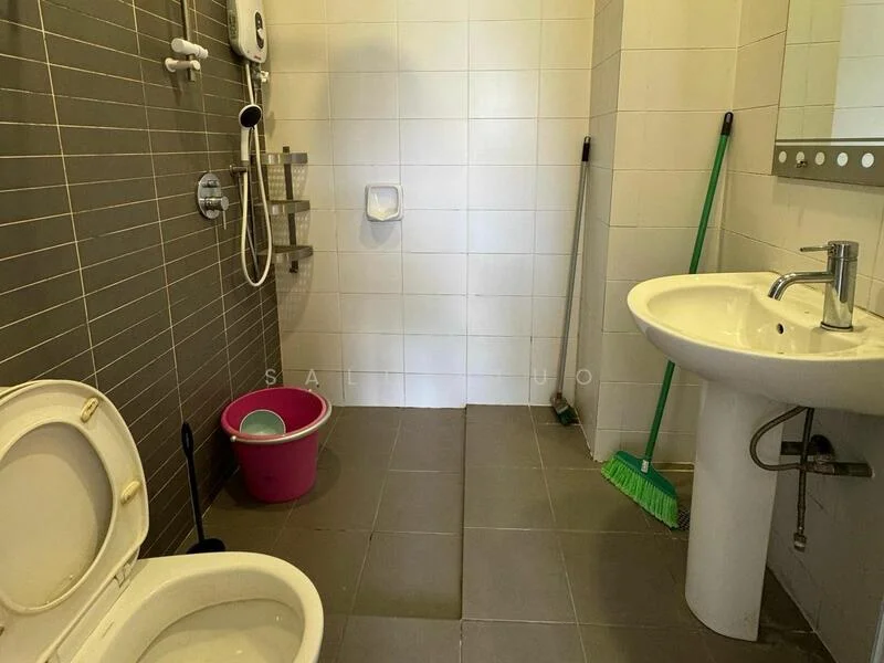 Bathroom features: white ceramic toilet, single-sink vanity with chrome faucet, mirror above sink, shower area with wall-mounted showerhead, handheld shower attachment, grey tiled walls, light grey floor tiles, cleaning supplies visible (broom and bucket).