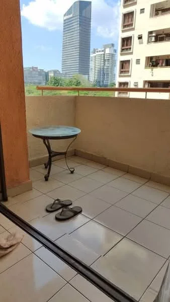 Balcony features: tiled flooring, glass railing, small round table, slippers on the floor, city skyline view; view: city.