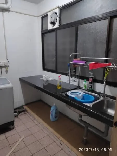 Laundry features: single-bowl stainless-steel sink, chrome pull-down faucet, black countertop, white tiled walls, pink dish rack, green dish drying mat, washing machine, window with black frames, tile flooring, cleaning supplies, blue plastic basin, detergent bottle.