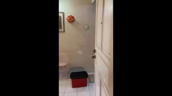 Room features: white painted walls, tiled flooring, wooden door, metal door handle, small stool, plastic storage box, decorative wall hanging.