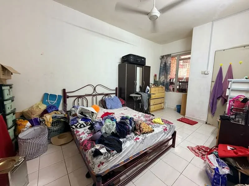 Bedroom features: queen-size bed with floral bedding, wooden bed frame, ceiling fan, white painted walls, tiled flooring, wardrobe with sliding doors, wooden dresser, plastic storage bins, clothes scattered on the floor, window with curtains, basket for laundry.
