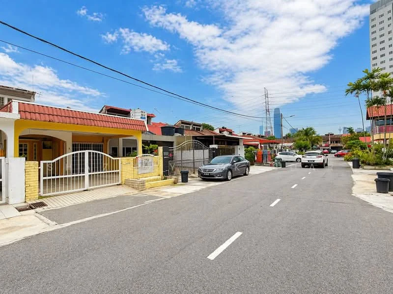 Exterior type: linked terrace house; features: red tiled roof, cream painted facade, white metal gate, paved driveway, surrounded by greenery, street view with parked cars, power lines visible, urban context with nearby buildings; style: modern.