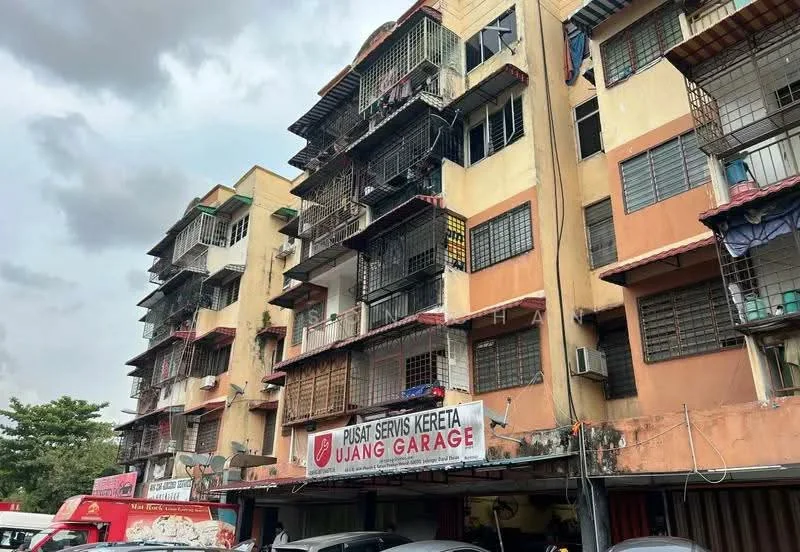 Exterior type: low-rise apartment block; features: cream painted facade, multiple balconies with metal railings, visible air conditioning units, ground floor commercial space, signage for car service, parking area in front, two-storey building, overcast sky; style: traditional.
