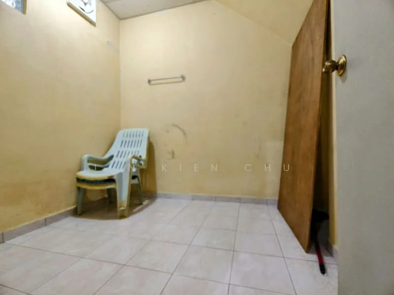 Room features: light yellow painted walls, white tiled flooring, single plastic chair, wooden door, wall-mounted towel rack, corner with exposed wall, no visible windows.