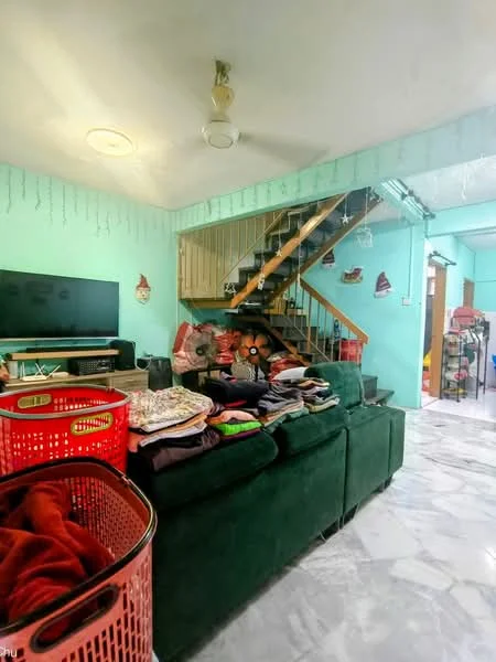 Living features: green fabric sofa, marble tile flooring, TV console, wall-mounted TV, decorative wall with hanging ornaments, staircase with wooden railing, basket of laundry, open layout to adjacent room.
