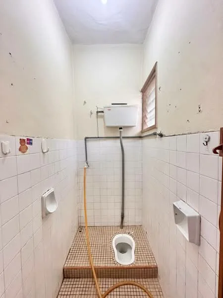 Bathroom features: white tiled walls, white tiled flooring, toilet, urinal, shower area, wall-mounted water heater, window for ventilation, hose for cleaning.