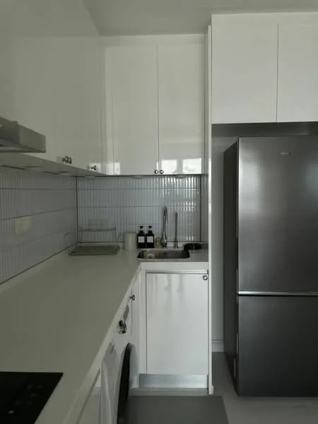 Kitchen features: white cabinetry with glossy finish, stainless-steel refrigerator, single-bowl stainless-steel sink, chrome pull-down faucet, white countertop, ceramic tile backsplash with vertical pattern, built-in oven, 4-burner electric hob, washing machine, under-cabinet lighting; style: modern.