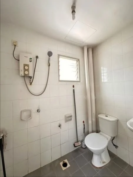 Bathroom features: white tiled walls, grey tiled flooring, one-piece toilet, shower with handheld showerhead, window for natural light, water heater, toilet paper holder, drain in floor.