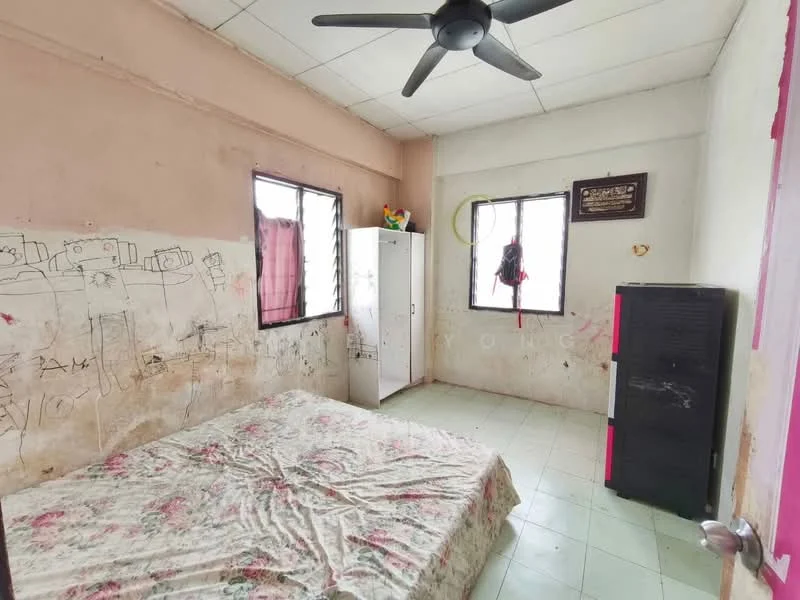 Bedroom features: queen-size bed with floral bedding, white walls with graffiti, two windows with metal grills, ceiling fan, green curtain, white wardrobe, black storage cabinet, green and red decorative items on the windowsill, tile flooring.