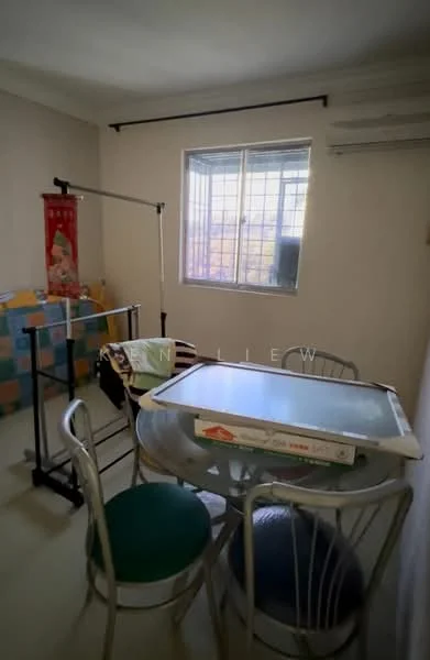 Room features: light-colored painted walls, window with grid design, flooring with light tiles, clothes rack, small round dining table, metal chairs with green cushions, air conditioning unit on wall, decorative wall hanging.