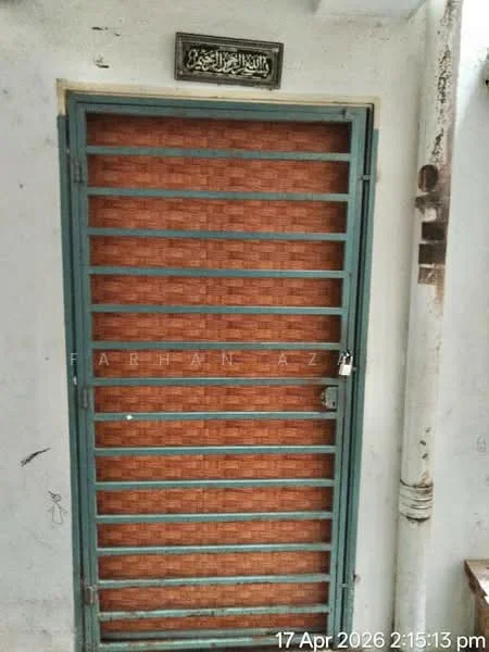 Room features: metal security door with horizontal bars, wooden paneling with a brick pattern, padlock on the door, decorative plaque above the door, white walls, visible pipe on the side.