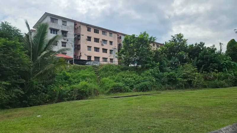Exterior type: low-rise apartment block; features: 3-storey building, painted facade in light pink and white, surrounded by greenery, manicured lawn in foreground, tropical landscaping, multiple windows visible, balconies on upper floors; style: modern.