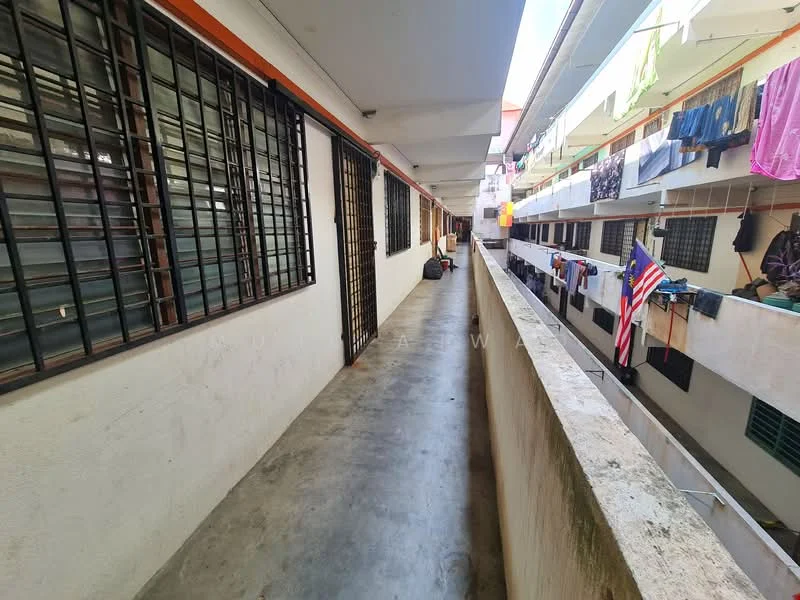 Room features: concrete flooring, white painted walls, metal grilles on windows, overhead lighting, balcony railing, laundry hanging on lines, clothes drying on balcony, visible corridor layout.