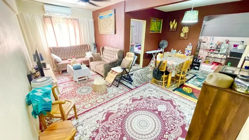 Living features: beige fabric sofa, brown fabric armchair, white coffee table, area rug with intricate pattern, ceiling fan, window with sheer curtains, decorative wall art, wooden side table, folding chair, dining table with patterned tablecloth, dining chairs, fan, kitchen area visible in background; style: contemporary.