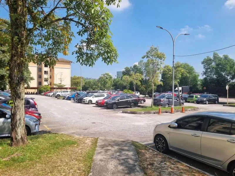 Exterior type: low-rise apartment block; features: open-air parking lot, manicured lawn, mature trees, paved driveway, multiple parked cars, surrounded by greenery, clear blue sky; style: modern.