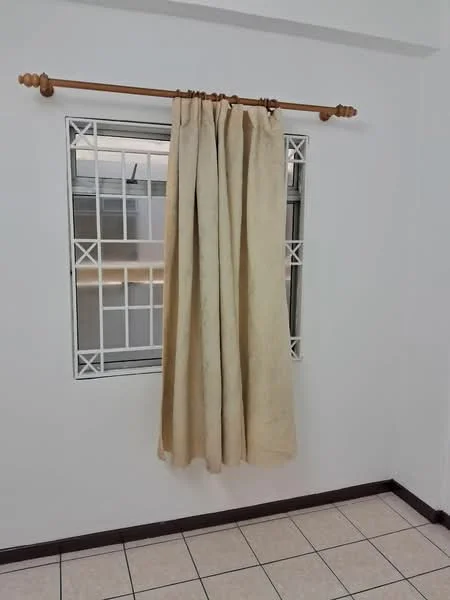 Room features: white painted walls, tile flooring, window with white grille, curtains in beige, wooden curtain rod.