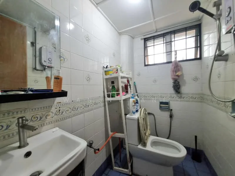 Bathroom features: white tiled walls, blue tiled flooring, single-bowl sink, chrome faucet, mirror above sink, toilet, shower area with handheld showerhead, shower curtain, shelf unit for toiletries, window for natural light.