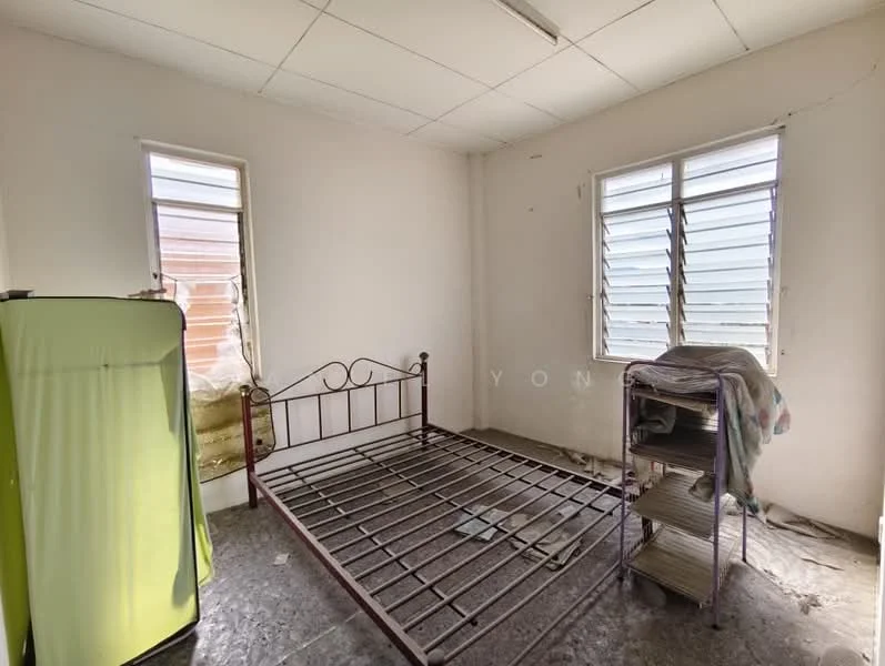 Bedroom features: single bed frame without mattress, green fridge, metal shelving unit, two windows with louvered shutters, white painted walls, grey flooring, exposed ceiling, minimal decor.