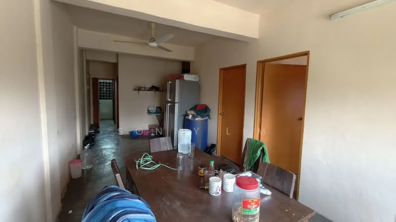 Dining features: wooden dining table, 4 wooden chairs, ceiling fan, refrigerator, wooden door, light-colored walls, concrete flooring, plastic water bottle, various food containers, green electrical cord. Room features: light-colored walls, concrete flooring, wooden door.