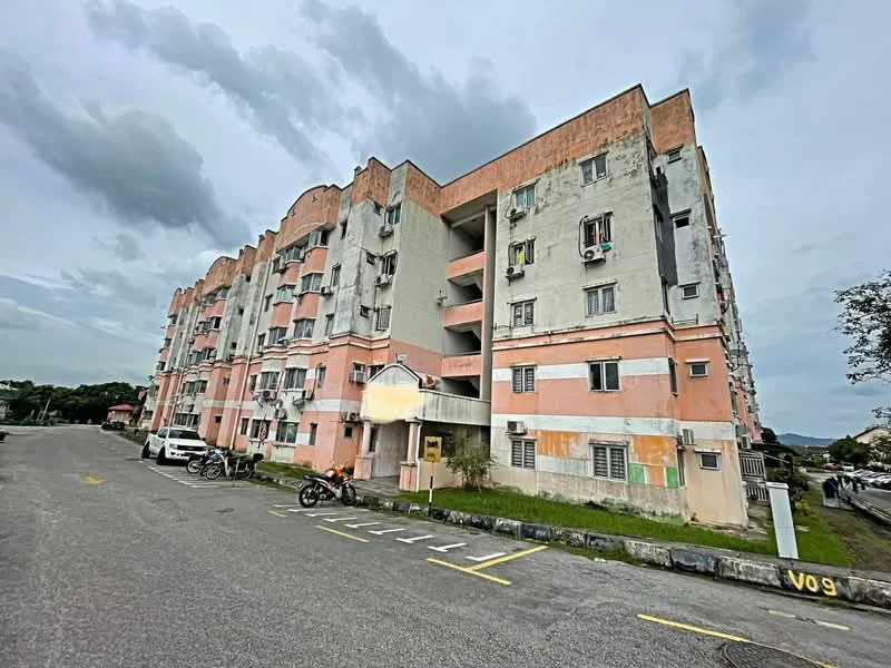 Exterior type: low-rise apartment block; features: pink and grey painted facade, exposed concrete, balconies with sliding doors, air conditioning units visible, parking spaces visible in front, surrounding greenery, multiple storeys, entrance with awning; style: modern.