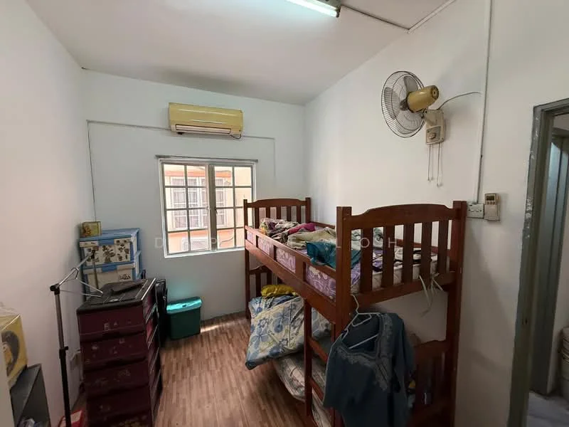 Bedroom features: bunk bed with wooden frame, single bed with bedding, wooden flooring, wall-mounted ceiling fan, window with grid pattern, air conditioning unit, green plastic storage bin, dresser with drawers, clothes hanging on the bed, decorative pillows.