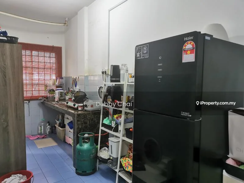 Kitchen features: black refrigerator, stainless-steel sink, granite countertop, white tiled backsplash, wooden cabinetry, gas stove, kitchen shelving, blue vinyl flooring, window with red grille, various kitchen utensils, green gas cylinder.
