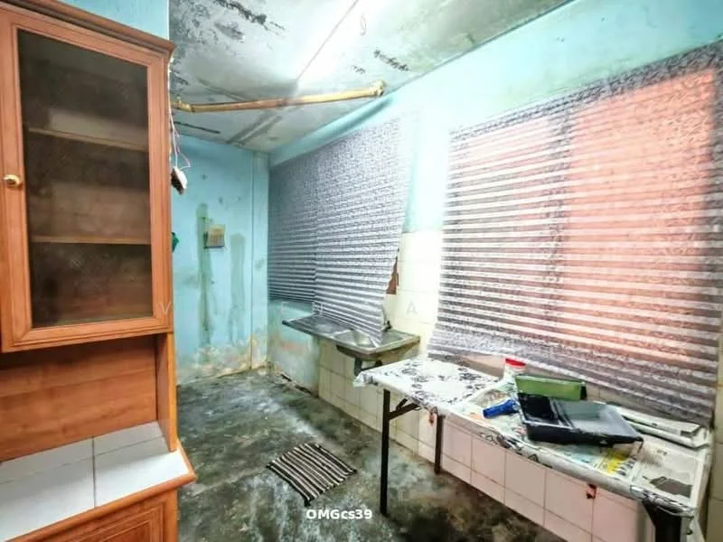 Kitchen features: blue painted walls, concrete ceiling, single-bowl stainless-steel sink, chrome faucet, window with blinds, wooden cabinetry, countertop with tiled surface, flooring with stains, kitchen mat, exposed plumbing, table with clutter.