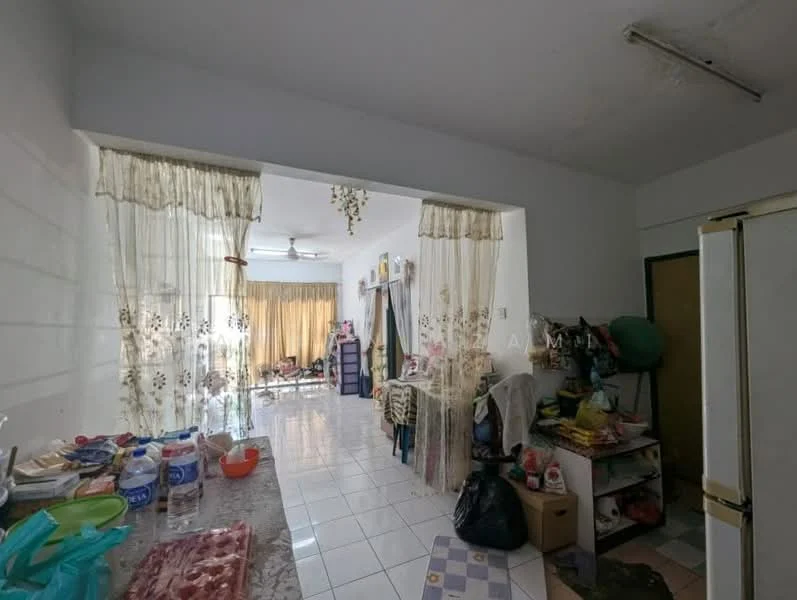 Room features: white painted walls, white tiled flooring, ceiling fan, curtains with floral pattern, kitchen countertop with granite surface, refrigerator, various kitchen items on countertop, open layout to living area, cluttered storage area, multiple chairs visible in living area.
