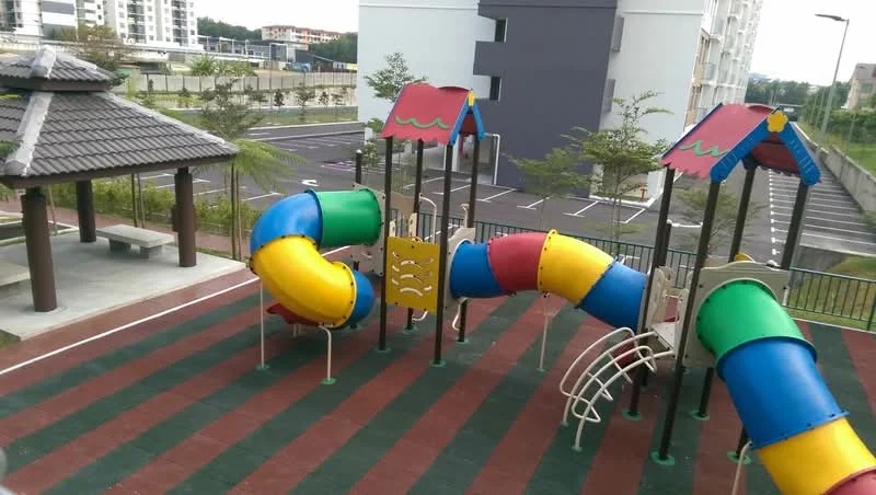 Exterior type: children's playground; features: colorful play structure with slides, climbing frame, sheltered seating area with roof, rubberized flooring, manicured landscaping, open space for play, surrounding parking area, fenced perimeter; style: modern.