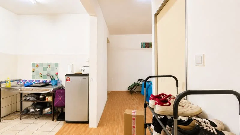 Room features: white painted walls, laminate flooring, stainless-steel fridge, kitchen countertop with tiled backsplash, metal shelving unit, stack of shoes on rack, open space leading to another room; style: modern.