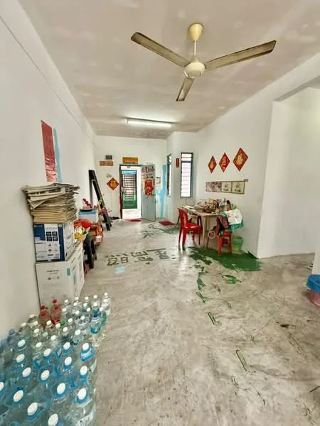 Room features: white painted walls, marble flooring, 5-blade ceiling fan, red plastic chairs, wooden table, stacked newspapers, bottled water, green paint splatters on floor, doorway leading to another room, decorative wall hangings; style: minimalist.