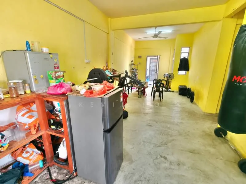 Room features: yellow painted walls, concrete flooring, ceiling fan, refrigerator, wooden shelving unit, plastic chairs, punching bag, various bags and items on the floor.