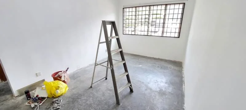 Room features: white painted walls, concrete flooring, large window with grid pattern, step ladder, bucket, paint supplies, unfinished space.