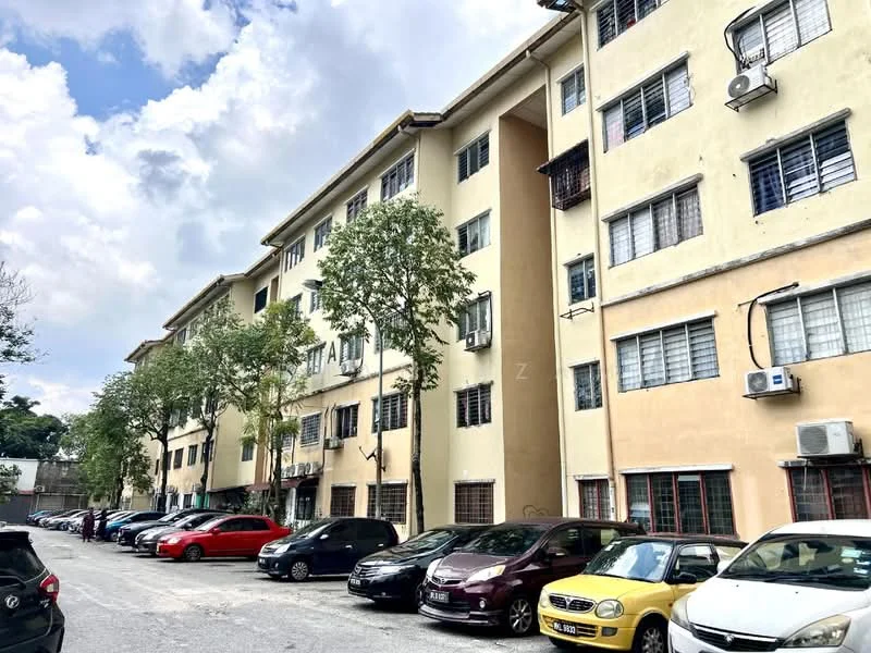 Exterior type: low-rise apartment block; features: yellow painted facade, 3-storey building, multiple windows with metal grilles, air conditioning units visible, trees in front of building, parking lot with multiple cars, asphalt driveway, surrounded by greenery; style: traditional.