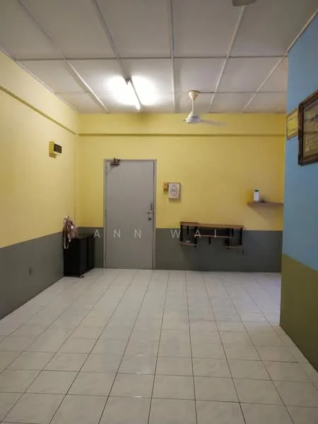 Room features: yellow painted walls, grey painted walls, white tiled flooring, ceiling with fluorescent lighting, ceiling fan, wooden shelf on wall, door leading to another room, black trash bin.